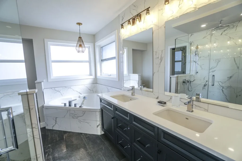 A modern bathroom featuring a double sink vanity with black cabinets, a large mirror, and sleek light fixtures. The room has a marble-tiled bathtub under a pendant light and a spacious shower, all bathed in natural light from a large window.