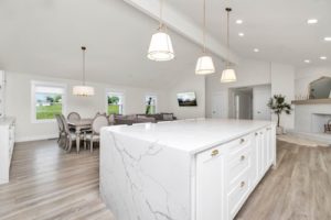 Experience the elegance of a spacious, modern kitchen that's perfect for those considering kitchen remodeling. Featuring a large marble island, pendant lights, and light wood flooring, it seamlessly flows into a dining area and living space with abundant natural light streaming through multiple windows.